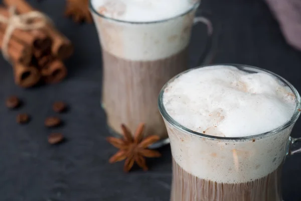 Café avec une riche mousse de lait dans un bécher de verre sur un fond sombre bâtons de cannelle et étoiles d'anis. Espace de copie — Photo