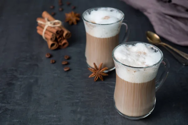 Coffee with rich milk foam in a glass beaker on a dark background sticks of cinnamon and stars of anise. Copy space — Stock Photo, Image