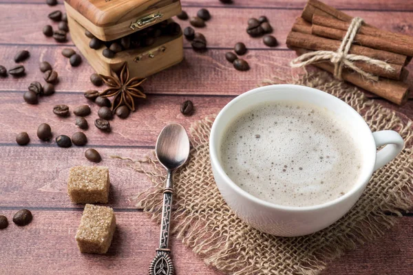 Witte koffie kop en schotel met melk schuim en rietsuiker kaneel anijs koffiebonen — Stockfoto