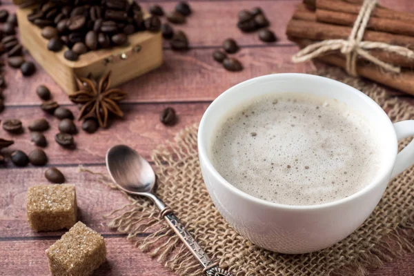 Weiße Kaffeetasse und Untertasse mit Milchschaum und Rohrzucker Zimtanis Kaffeebohnen — Stockfoto