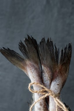 Raw fish tails tied with rope with bow on dark background. Selective focus clipart