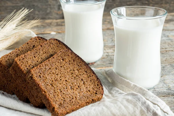 Frische gesunde Milch in Glasbechern und geschnittenes Getreidebrot auf rustikalem Holzgrund — Stockfoto