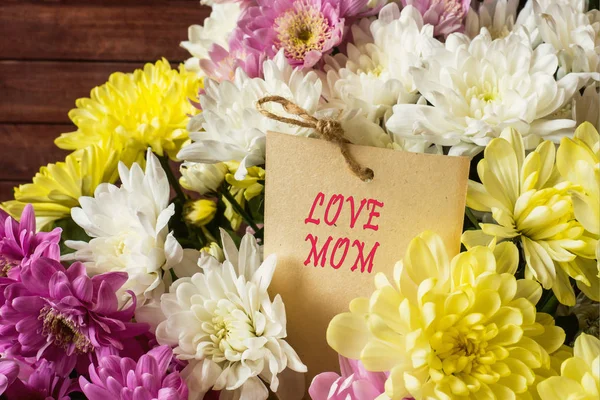 Inscription Love Mom. Bouquet of multicolored chrysanthemums on brown wooden backgroun — Stock Photo, Image