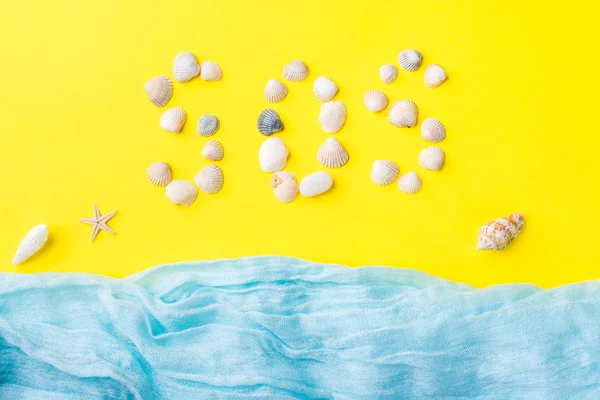 El concepto de vacaciones de verano. Conchas de mar fondo amarillo Bufanda azul imitación mar Texto de conchas SOS — Foto de Stock