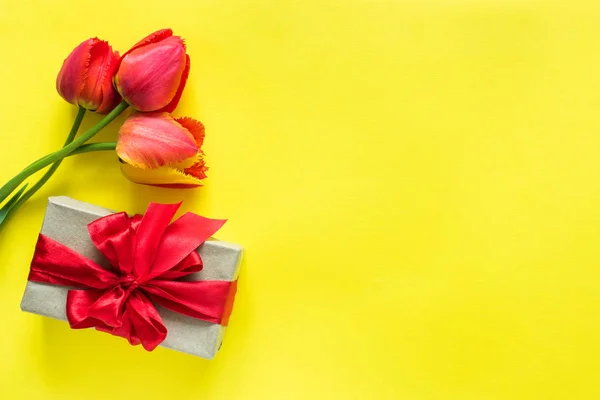 礼品盒与红丝带弓花花束郁金香在明亮的黄色背景复制空间文本 — 图库照片
