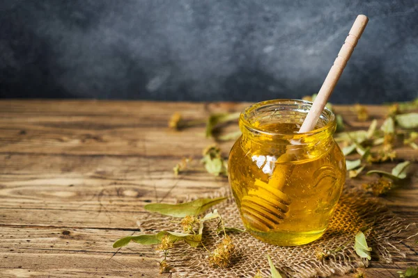 Un pot de miel liquide de fleurs de tilleul et un bâton de miel — Photo