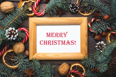 Noel ağacı konilerinin çerçevesi koyu ahşap arka planda karamel kamışlı fındıklar. Yazıt Mutlu Noeller