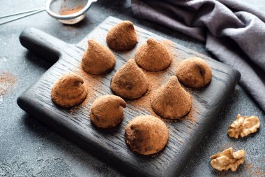 Tahta bir standın üzerine kakao tozu ve ceviz serpiştirilmiş lezzetli çikolatalı trüf mantarları. Koyu beton arkaplan.