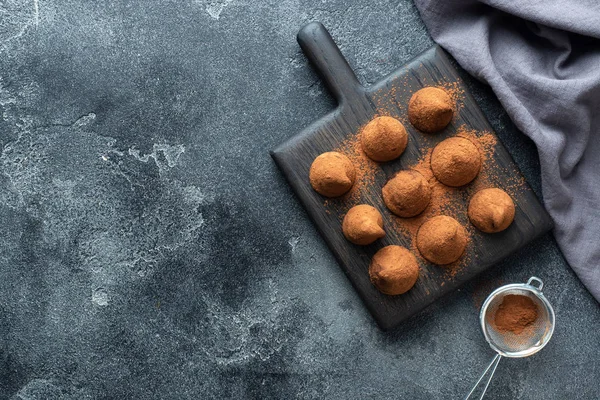 Deliciosas trufas de chocolate polvilhadas com cacau em pó e nozes em um suporte de madeira. Fundo de concreto escuro. Espaço de cópia . — Fotografia de Stock