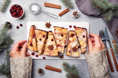 Dişi eller, içinde kızılcık ve üzerine pudra şekeri serpiştirilmiş baharat serpiştirilmiş süzme peynirli turta güveci olan bir standı tutuyor. Gri beton masa.