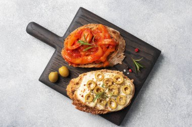 Krem peynirli tam tahıllı sandviç, zeytin ve ahşap kesim tahtasında domatesli konserve biber. Boşluğu kopyalayan gri beton arkaplan.