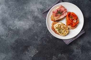 Krem peynirli, pastırmalı, biberli ve domatesli tam tahıllı sandviç. Boşluğu kopyalayan koyu beton arkaplan.