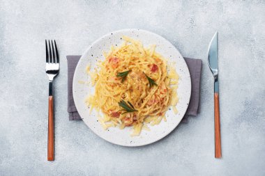 Baharatlı bir tabakta pastırmalı yumurta peynirli makarna. Geleneksel İtalyan yemeği Carbonara. Gri beton masa. Boşluğu kopyala.