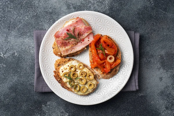 Бутерброды со сливочным сыром, беконом и оливковым перцем с помидорами на тарелке. Темно-бетонный фон с копированием пространства . — стоковое фото