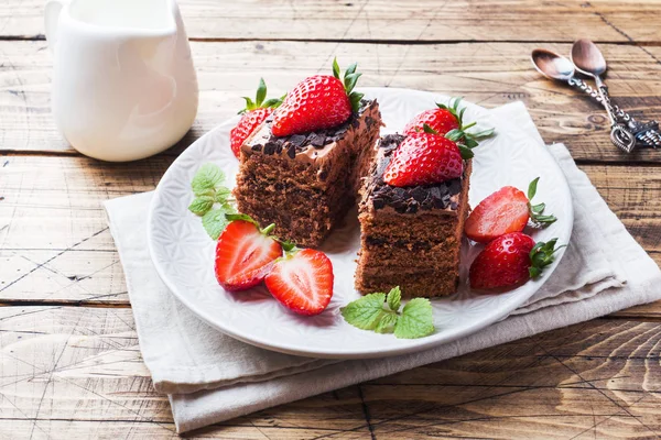 Chocolate truffle cake with strawberries and mint. Wooden table.