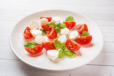 Beyaz tabakta domates, mozzarella peyniri ve Fesleğen caprese salatası. İtalyan mutfağı.