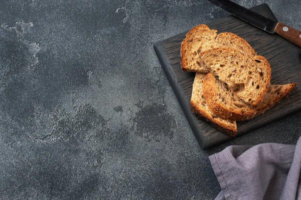 Scheiben Vollkornbrot auf einem Holzschneidebrett. dunkler Betonhintergrund. Kopierraum — Stockfoto