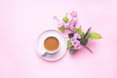 Sütlü bir fincan kahve ve çiçek ve yapraklı bir dal. Fotokopi alanı olan pembe bir pastel arka planda. Düz yatıyordu.