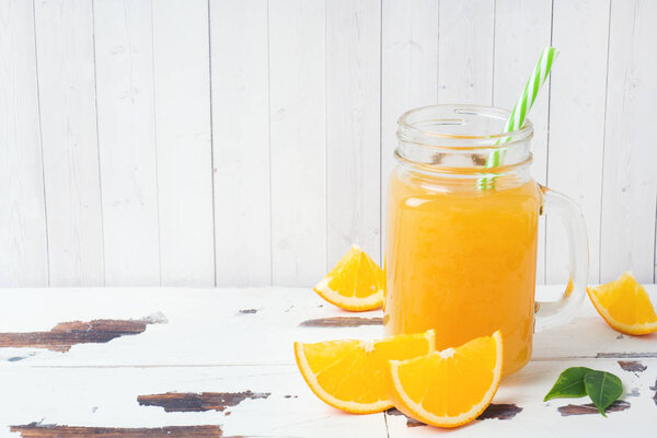 Orange juice in glass jars and fresh oranges on a white wooden rustic background.