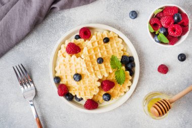 Beton bir arka plan üzerinde taze ahududu ve yaban mersini ile oluklu waffle çerezleri. Kopyalama alanı.