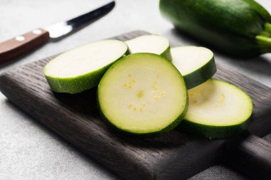 Kesme tahtasında dilimlenmiş taze yeşil kabak. Somut gri arka plan. Kapat..