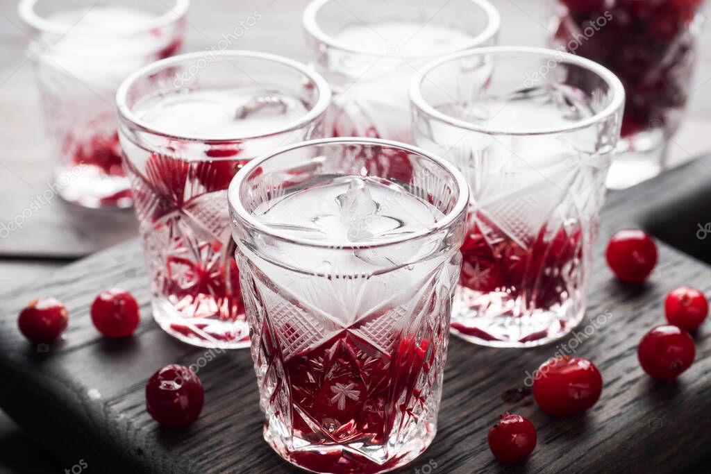 Stacks of vodka and cranberries on a wooden stand and background. Copy of the space. Bar alcoholic beverage tincture.
