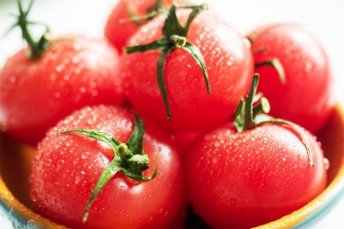 Bir tabak suyun içinde taze kırmızı kiraz domatesleri. Seçici odak.