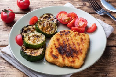 Izgarada kızarmış tavuk ve kabak şnitzel. Tabakta taze domates. Lezzetli bir yemek hazırlayın. Ahşap arkaplan