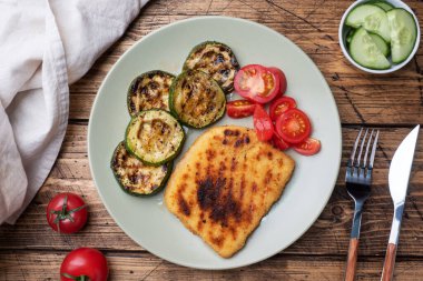 Izgarada kızarmış tavuk ve kabak şnitzel. Tabakta taze domates. Lezzetli bir yemek hazırlayın. Ahşap arkaplan