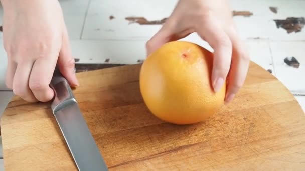 Žena krájí grapefruit na dřevěné desce domácí kuchyně. Užitečné zdravé potraviny plody citrusů. — Stock video