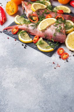 Limon dilimleri, dereotlu yeşillikler ve beton zeminde kırmızı acı biberli çiğ balık tüneği. Uzayı kopyala Sağlıklı gıda ve diyet konsepti. Balık pişirmek için gerekli malzemeler