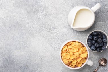 Doğal mısır gevreğinden taze yaban mersini, bal ve sütle yapılmış mısır gevreği. Sağlıklı sağlıklı bir kahvaltı konsepti. Boşluğu kopyala Gri arkaplan.