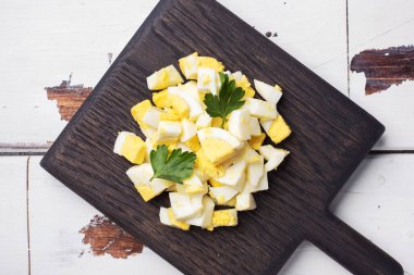 Haşlanmış tavuk yumurtası ahşap bir tahtada maydanoz yapraklarıyla ince ince doğranmış.