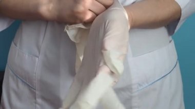 Beyaz önlüklü bir doktor ellerine lateks eldiven takıyor.