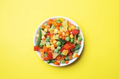 Sarı arka planda bir tabakta dondurulmuş sebzeler. Mısır bezelyeli havuç. Boşluğu kopyala