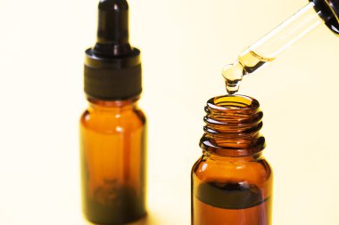 Damlalar pipetten düşer. Sarı arka planda pipetli bir şişe kozmetik yağı. Uzayı kopyala Seçici odak