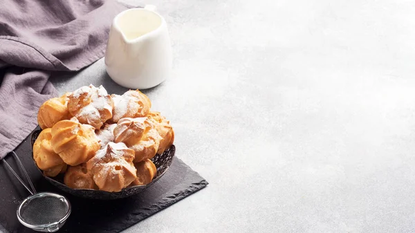 stock image Profiteroles with custard and powdered sugar on a plate. Concrete grey table. Copy space