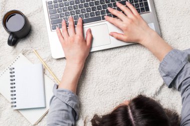 Beyaz yün battaniyeye uzanmış bilgisayar başında çalışan bir kadın. Evde çalışma ve öğrenme kavramı. Boşluğu kopyala