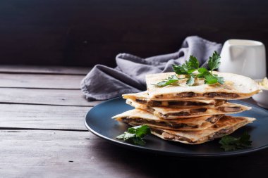 Peynirli ve mantarlı Quesadilla parçaları maydanoz yapraklı bir tabakta. Ahşap arkaplan kopyalama alanı