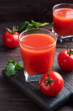 Cam bardakta domates suyu ve dalda taze olgun domates. Kopya alanı olan koyu tahta arkaplan