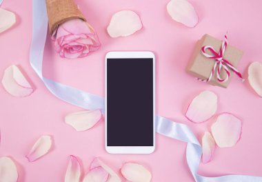 Pastel arka plan üzerinde pembe yaprakları ile Smartphone.