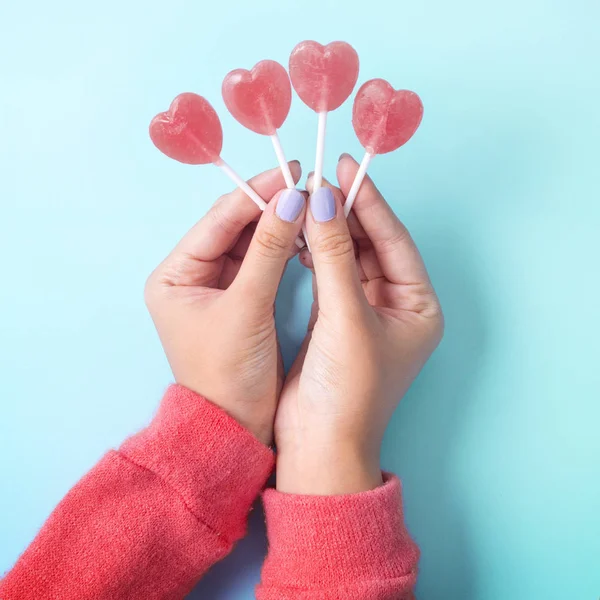 Sosteniendo caramelos de paleta en forma de corazón de San Valentín en el cielo backg azul —  Fotos de Stock