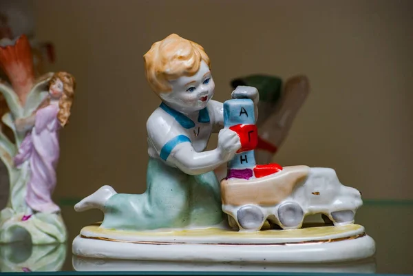 Figurinha de porcelana rara em uma prateleira de vidro. Menino brincando com brinquedos — Fotografia de Stock