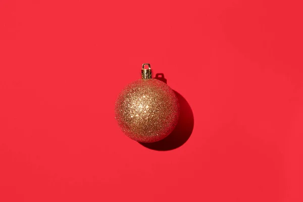 Goldglänzende Weihnachtskugel auf rotem Hintergrund. Stockbild