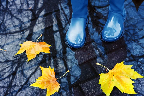 Woman in blue rain boots standing in puddle