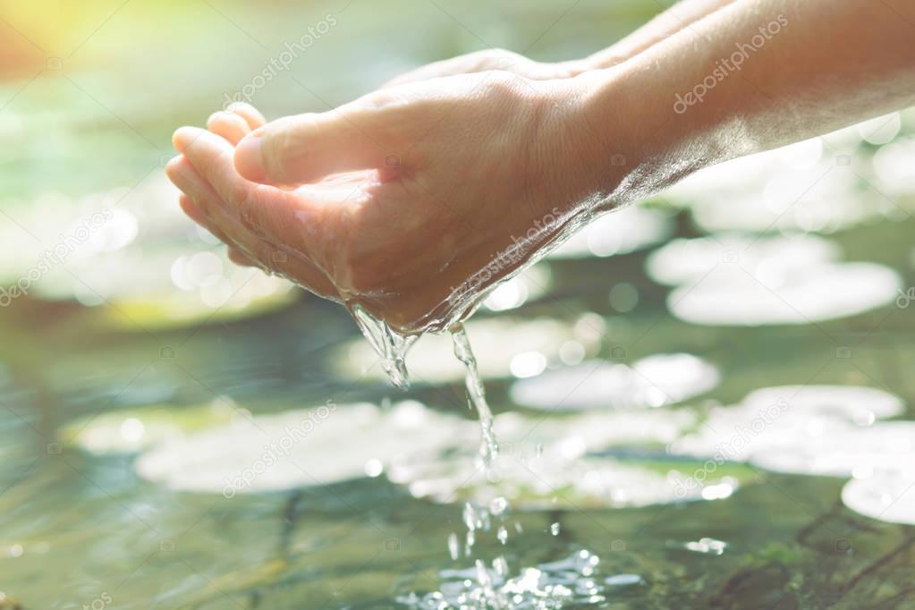 Hands in cupped form getting water from a lake or fountain