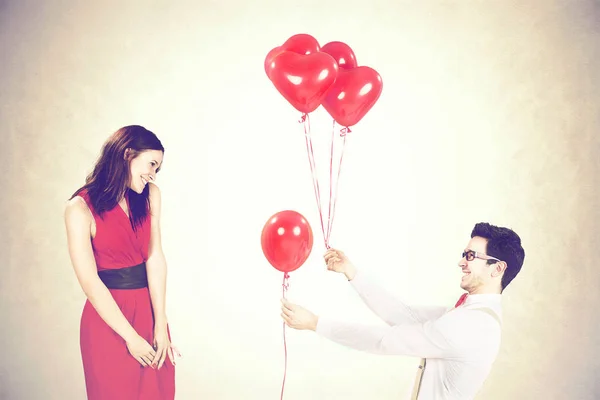 Mann nähert sich Frau und gibt ihr rote Luftballons in Herzform an einem Valentinstag — Stockfoto