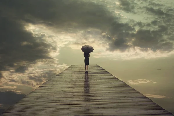 Donna misteriosa con ombrello attraversa un ponte verso il cielo minaccioso — Foto Stock