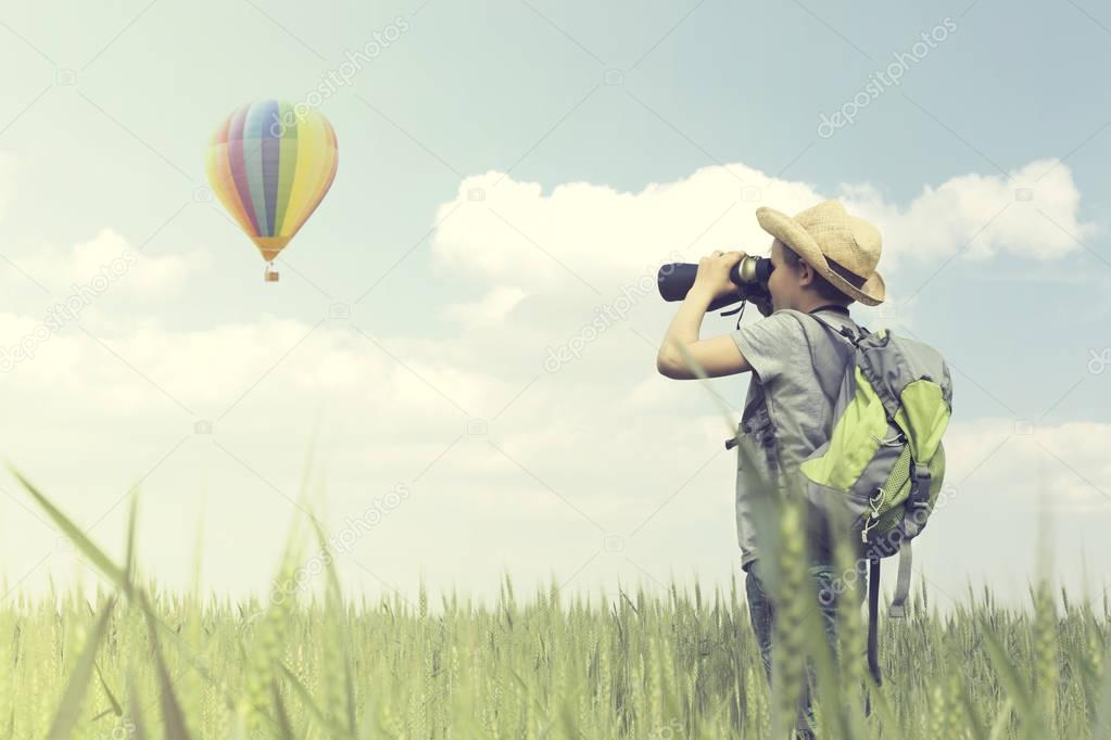 Child looks curious with his binoculars a hot air balloon flying in the sky