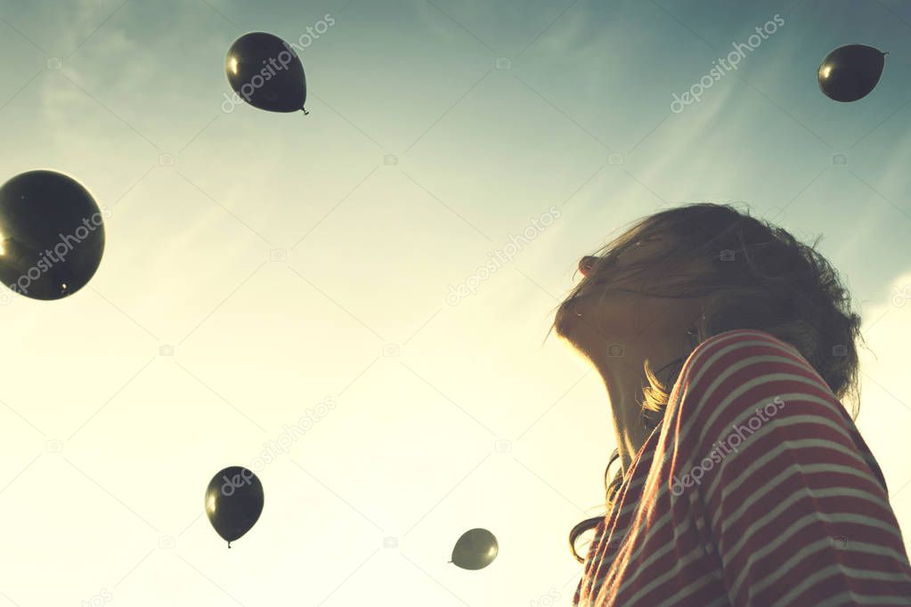 Surreal moment, woman looks surprised with a rain of black balloons falling from the sky